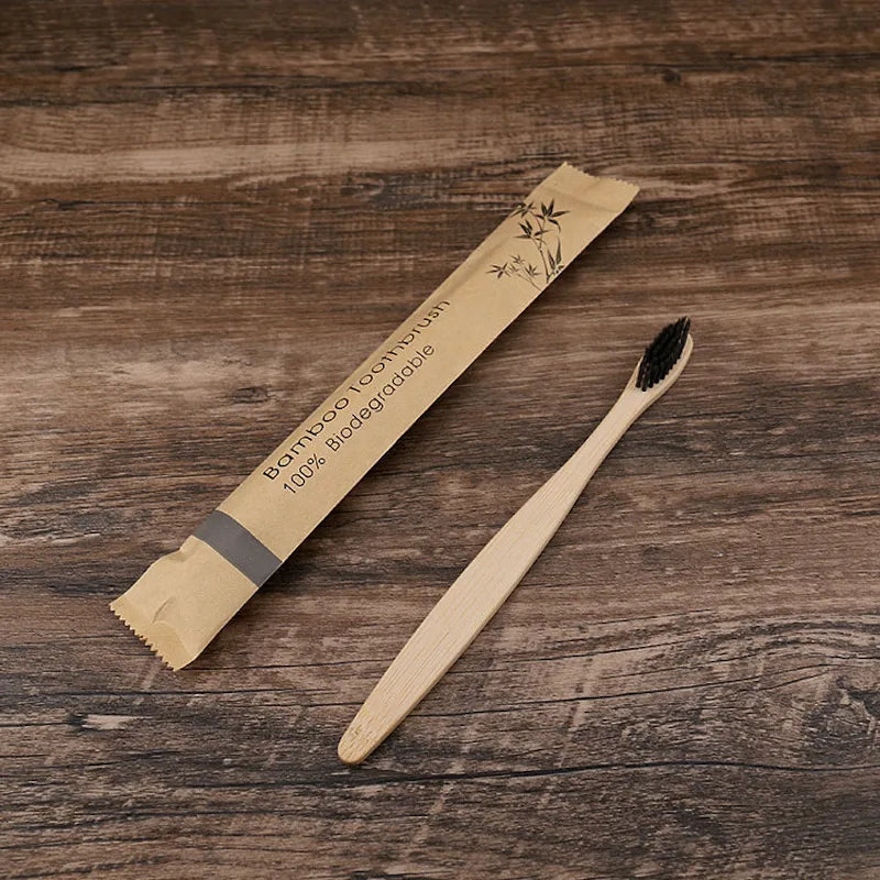 Sustainable bamboo toothbrush with black bristles shown next to its biodegradable kraft paper packaging on a wooden background