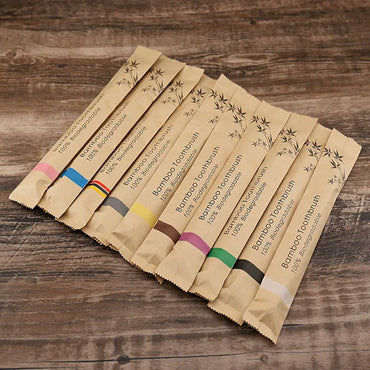 Set of biodegradable bamboo toothbrushes in individual kraft paper packaging with color-coded labels, arranged on a wooden surface