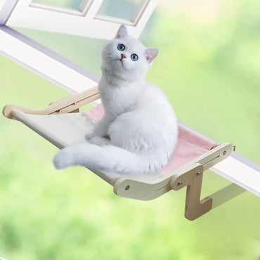White cat sitting on a pink window-mounted hammock bed enjoying an elevated view through the glass.”