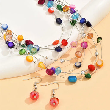 Close-up of multicolor shell necklace with matching red crystal earrings on a pastel background
