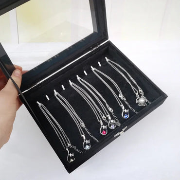 Hand opening a black display box showcasing silver necklaces with colorful crystal gemstone pendants