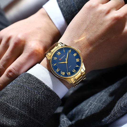 CURREN gold-tone men’s quartz watch with blue Roman numeral dial on wrist