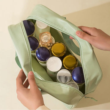Top view of a green matte translucent toiletry bag unzipped and filled with bottles and skincare items, held by two hands