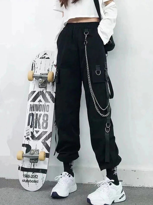 Woman wearing black Harajuku-inspired high-waist cargo joggers with chain and pocket details, styled with sneakers and a skateboard.