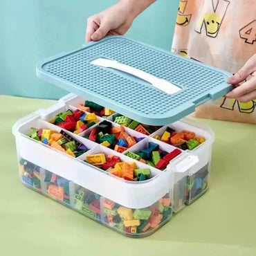 Transparent plastic Lego-compatible storage box with lid and built-in handle, showing color-coded divider grid filled with building blocks"