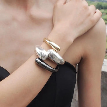 Woman wearing a modern metal cuff bracelet set by MANILAI featuring chunky gold, silver, and black bangles with a bold fashion-forward design
