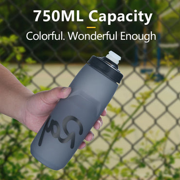 Hand holding a 750ml Rapha sports water bottle in front of a fence, showcasing its squeeze-to-drink design and leak-proof nozzle