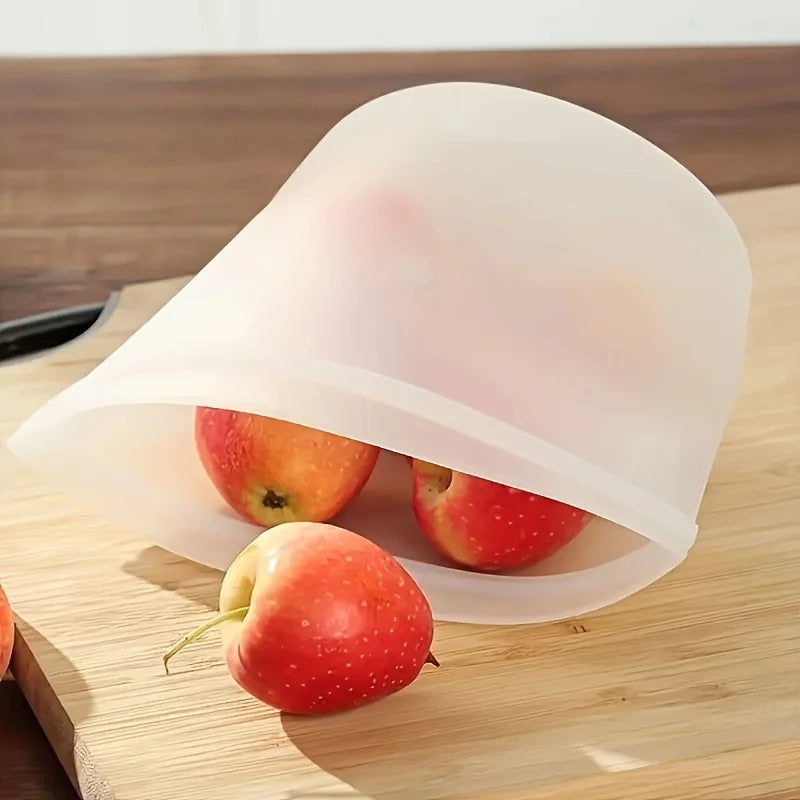 Transparent reusable silicone food storage bag holding fresh apples on a wooden cutting board—ideal for storing fruits and snacks