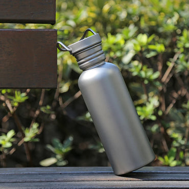 titanium water bottle leaning against bench outdoors with green foliage in background