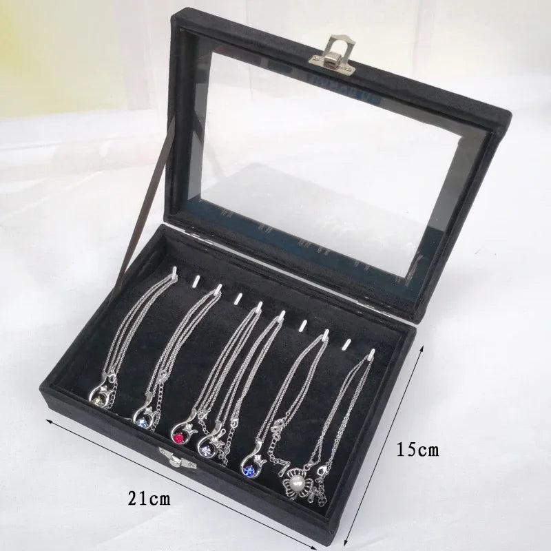 Black velvet jewelry display box with transparent glass lid, holding silver necklaces, measuring 21cm by 15cm
