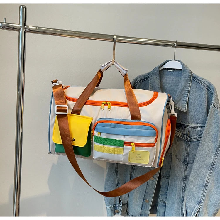Colorblock nylon duffel bag with orange zippers and brown straps hanging on a clothing rack next to a denim jacket, showcasing compact and stylish design