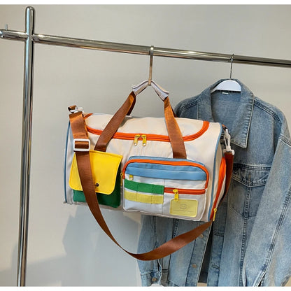 Colorblock nylon duffel bag with orange zippers and brown straps hanging on a clothing rack next to a denim jacket, showcasing compact and stylish design
