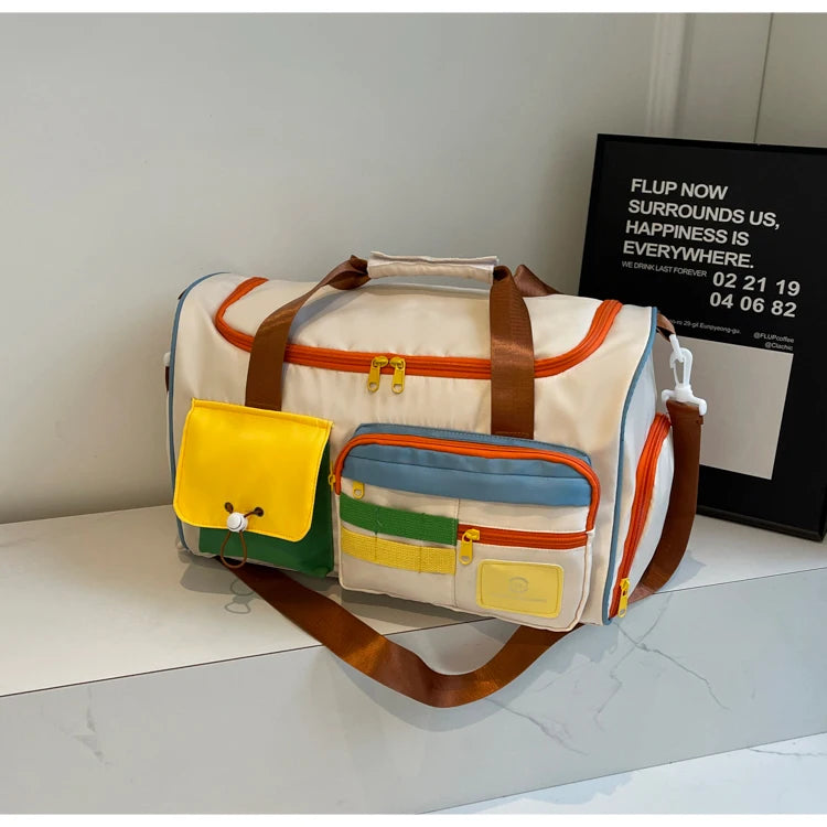 Colorblock nylon duffel bag with brown straps, orange zippers, and colorful front pockets, displayed on a white surface with framed wall art in background