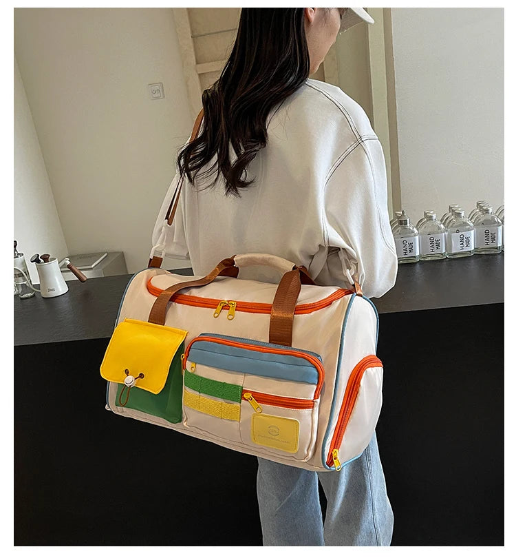 Woman wearing a casual outfit carrying a white nylon duffel bag with colorful front pockets and orange zippers, styled for travel or gym use