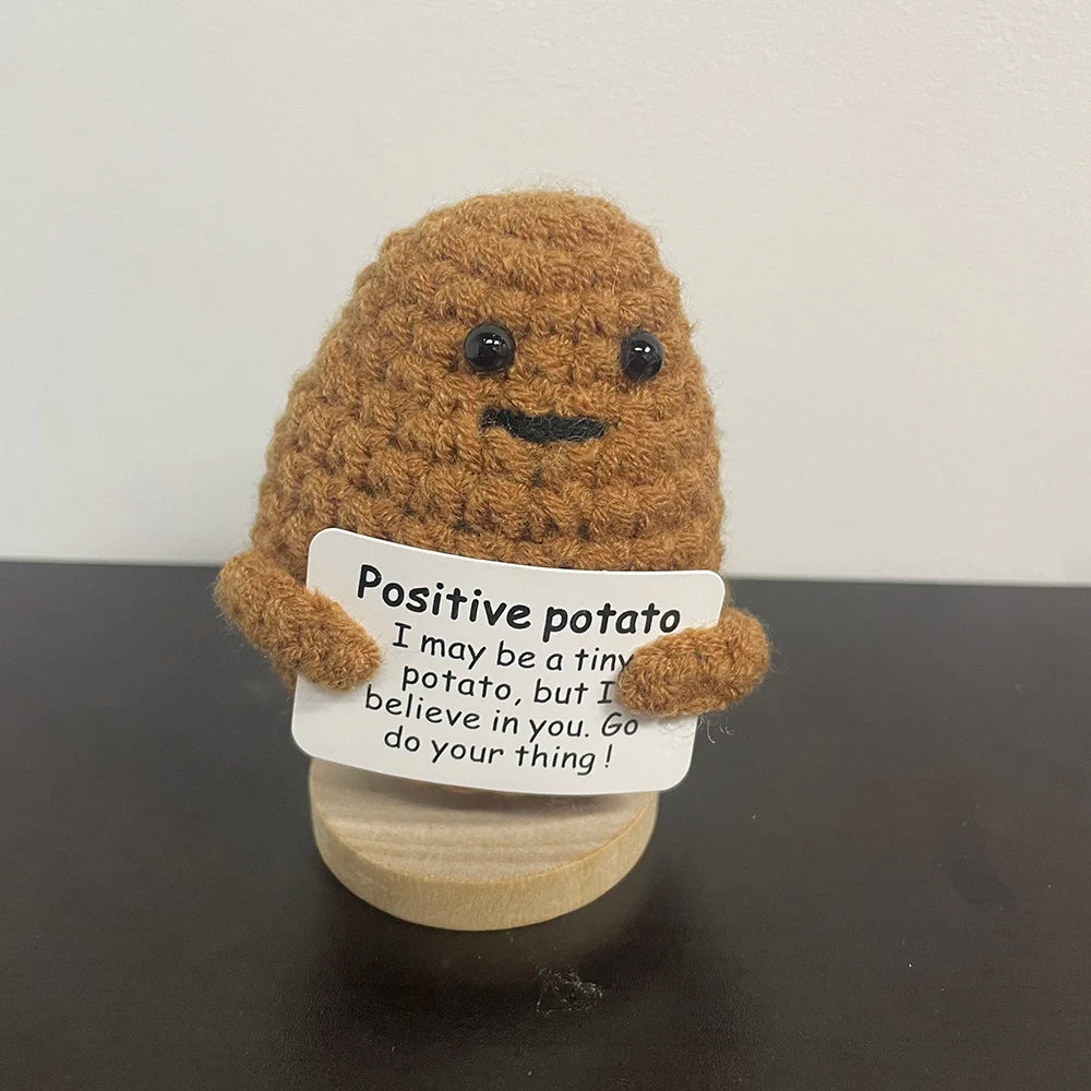 Handmade crochet potato plush doll with a smiling face, holding a sign that says "Positive potato – I may be a tiny potato, but I believe in you. Go do your thing!