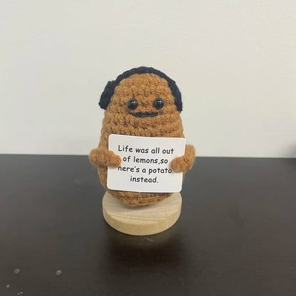 Handmade crochet potato plush doll with black mustache and hair, holding a sign that says "Life was all out of lemons, so here’s a potato instead