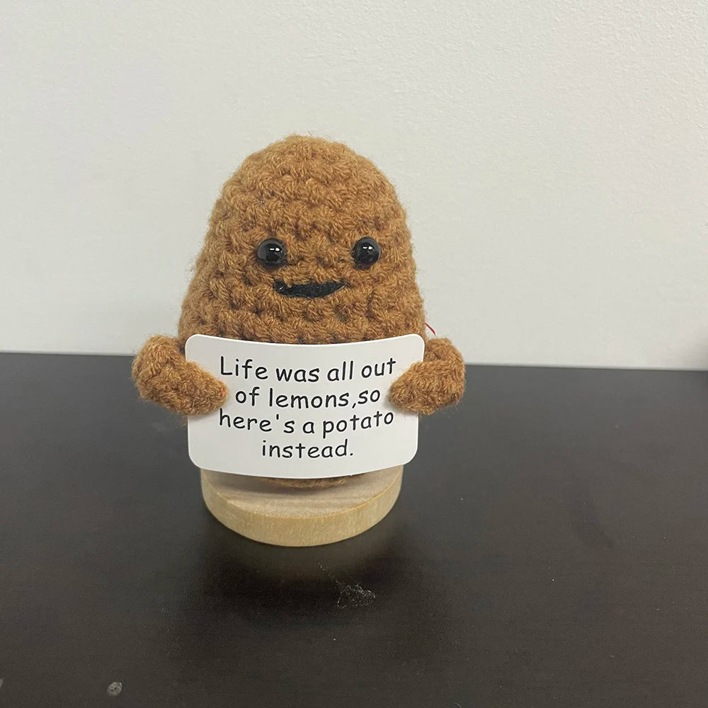 Handmade crochet potato plush doll with smiling face, holding a sign that says "Life was all out of lemons, so here’s a potato instead.