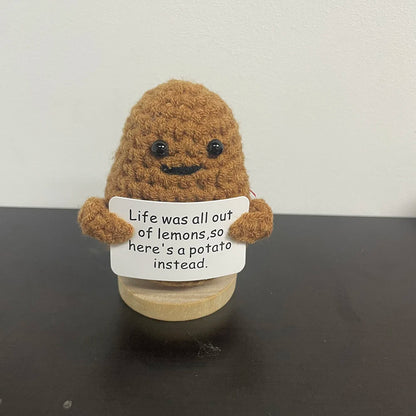 Handmade crochet potato plush doll with smiling face, holding a sign that says "Life was all out of lemons, so here’s a potato instead.