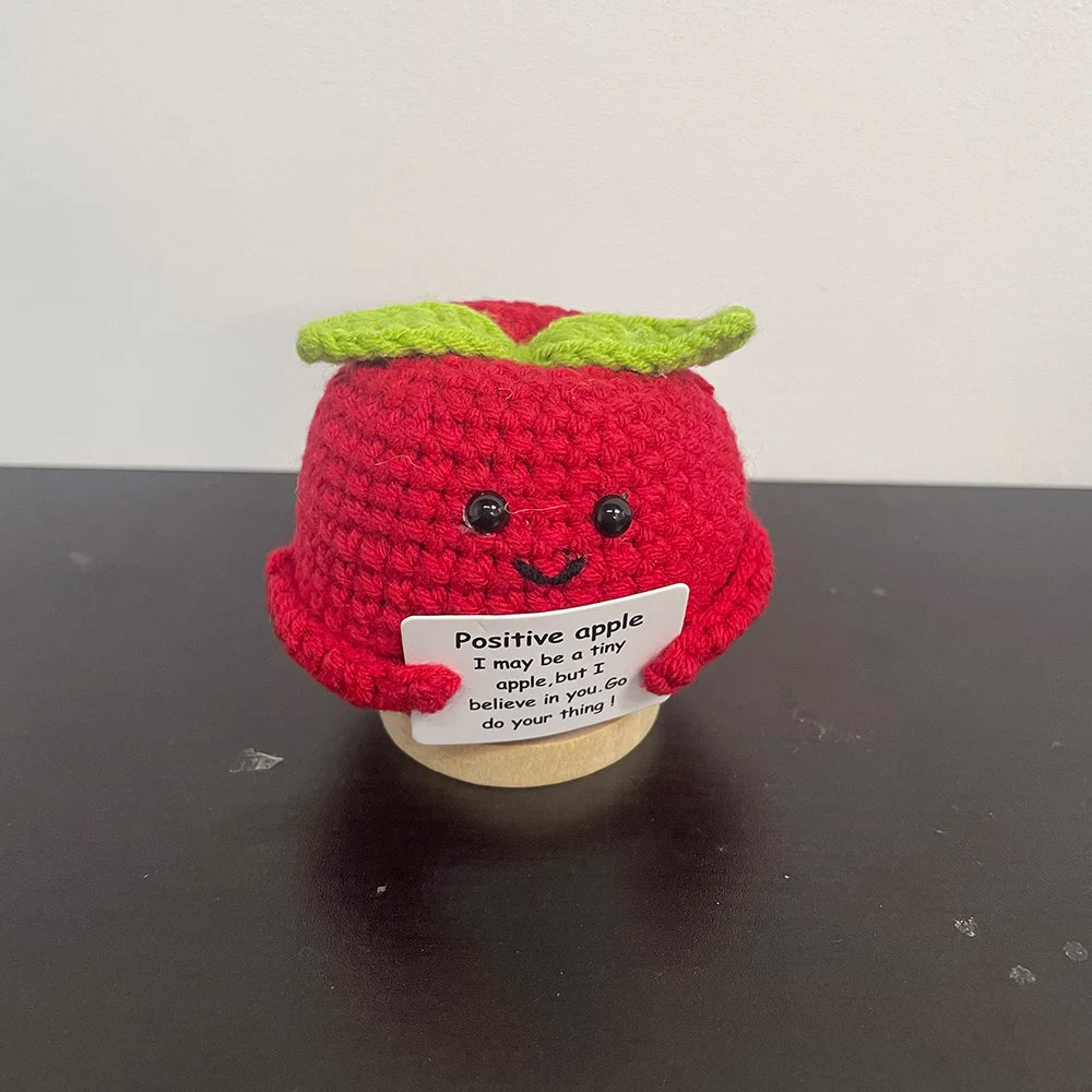 Handmade crochet apple plush with smiling face holding sign that says 'I may be a tiny apple, but I believe in you' — cute desk decor and inspirational gift