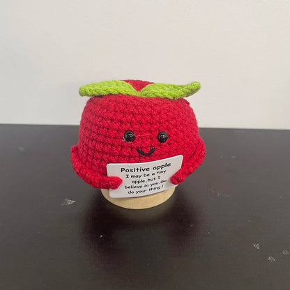 Handmade crochet apple plush with smiling face holding sign that says 'I may be a tiny apple, but I believe in you' — cute desk decor and inspirational gift