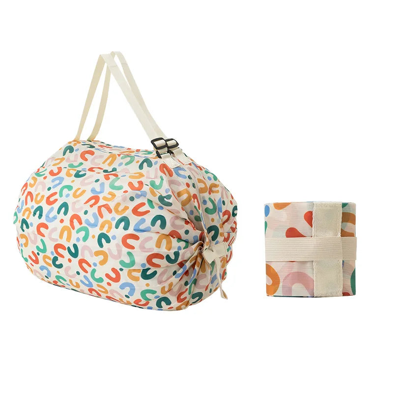 Colorful abstract print Oxford shopping bag with cream straps, shown alongside its neatly folded version secured with a matching strap.  BeTrendy