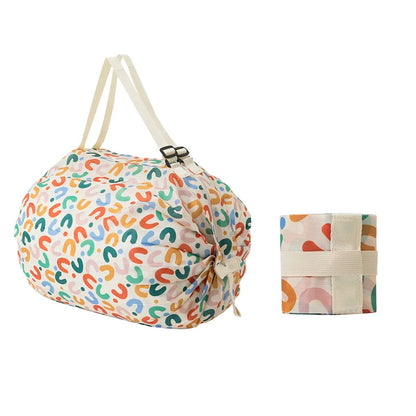 Colorful abstract print Oxford shopping bag with cream straps, shown alongside its neatly folded version secured with a matching strap.  BeTrendy