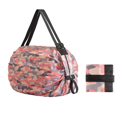Large pink camouflage Oxford shopping bag with black straps shown next to its compact folded version secured with an elastic band.  Berendy