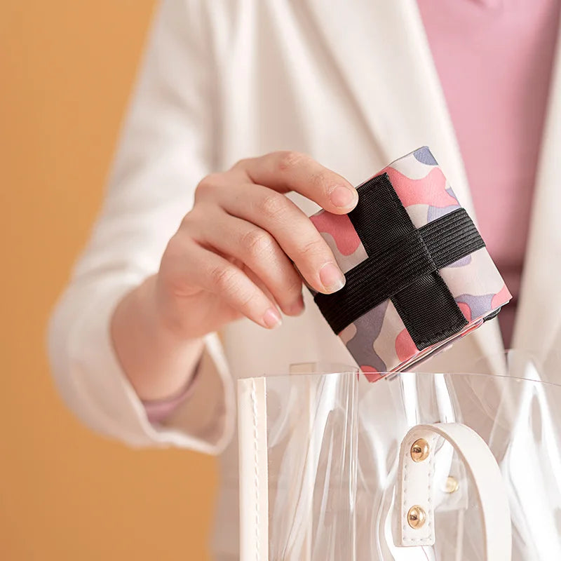 Woman placing a folded pink camouflage Oxford shopping bag into a clear handbag, showcasing its compact and portable design.  BeTrendy