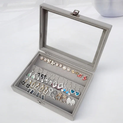 Gray velvet jewelry display box with transparent lid showing assorted colorful earrings in various designs