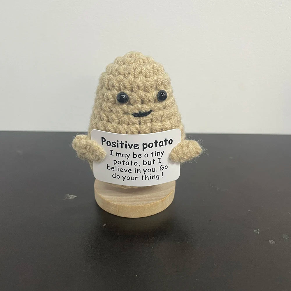 Light tan handmade crochet potato plush doll with smiling face, holding a sign that says "Positive potato – I may be a tiny potato, but I believe in you. Go do your thing!