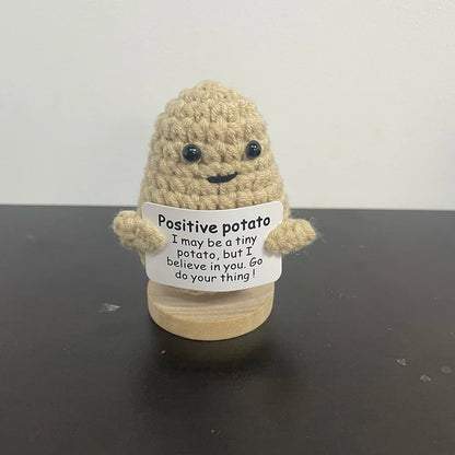 Light tan handmade crochet potato plush doll with smiling face, holding a sign that says "Positive potato – I may be a tiny potato, but I believe in you. Go do your thing!
