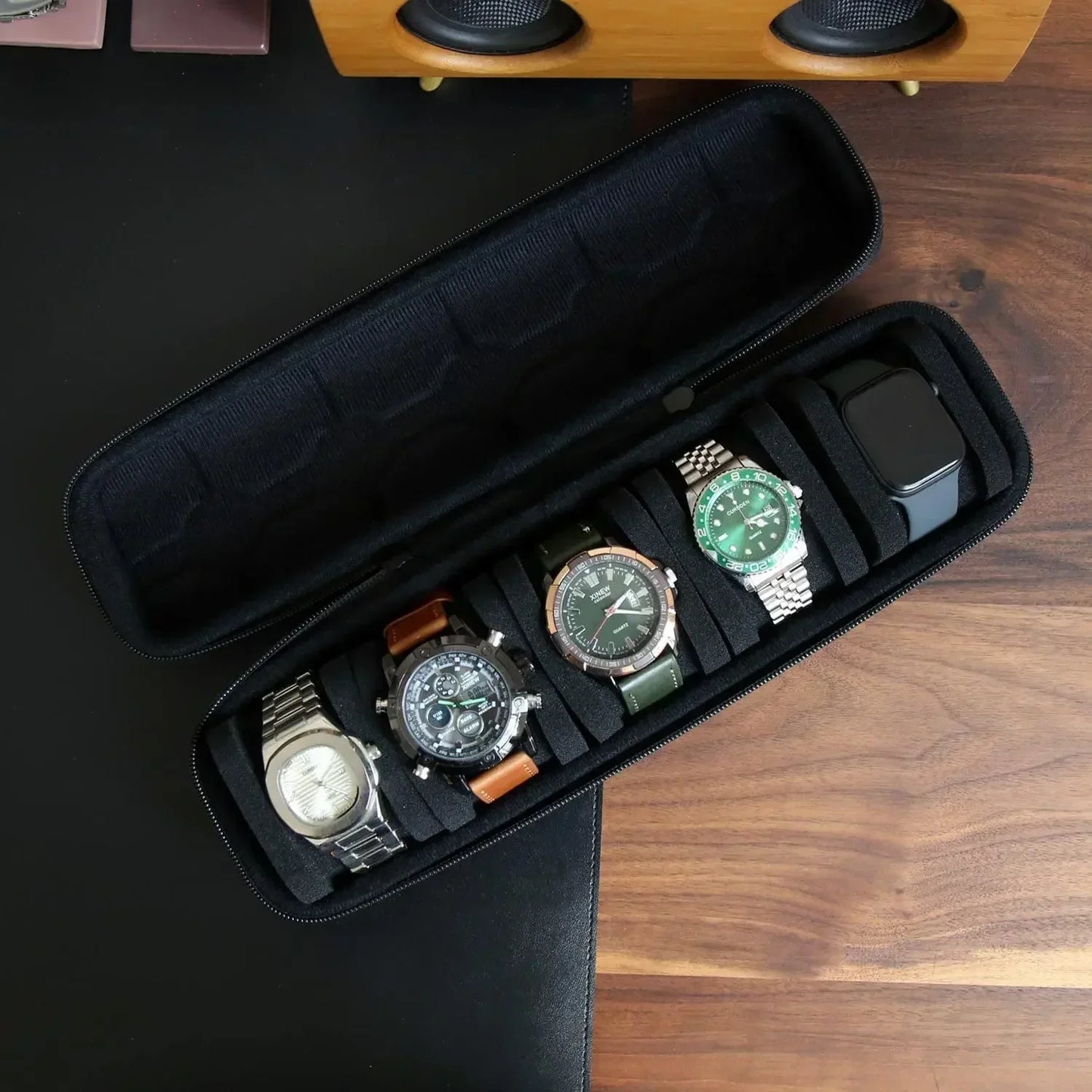 Long black zippered watch case open to show five different wristwatches securely placed in foam slots on a wooden surface
