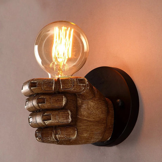 Nordic resin wall lamp shaped like a hand holding an exposed bulb, mounted on a circular black base with warm industrial lighting glow