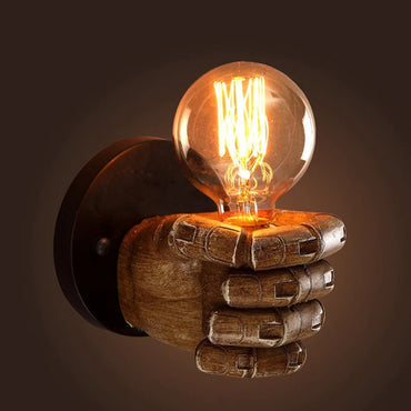 Wood-textured resin hand wall lamp holding an illuminated Edison bulb against a dark background, creating a warm ambient glow in industrial style