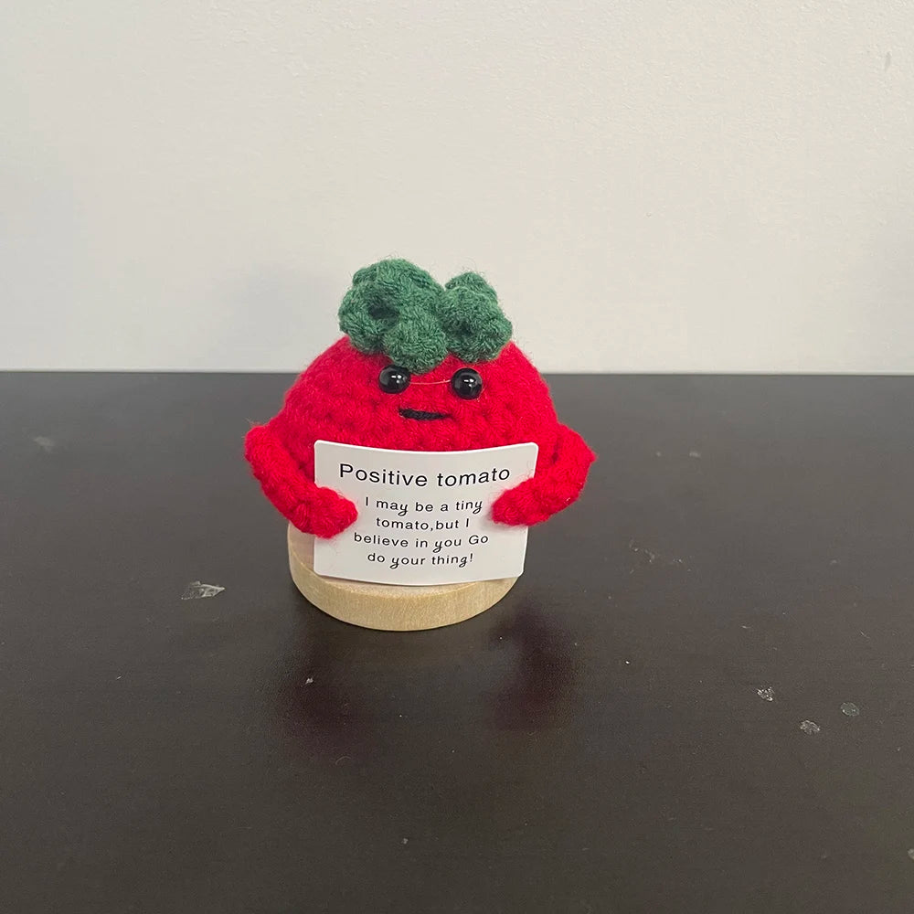 Red crochet tomato plush doll with green top, holding a sign that says "Positive tomato – I may be a tiny tomato, but I believe in you. Go do your thing!