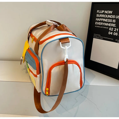 Side view of colorblock nylon duffel bag with orange zippers, blue trim, and brown adjustable strap, showing curved end pocket design