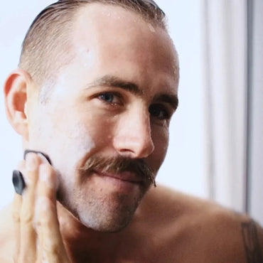 Man gently cleansing face with silicone grooming brush during skincare routine