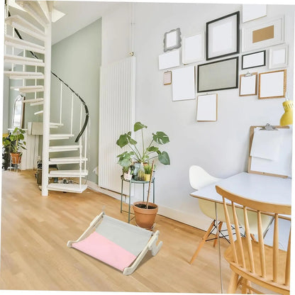 Window-mounted wooden cat hammock in a minimalist home with plants and spiral staircase in the background.